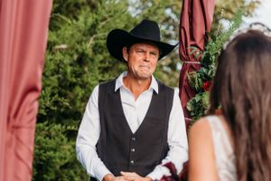 Officiant in western attire conducts ceremony under coral-colored draping at outdoor venue.
