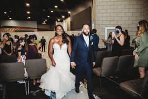 Joyful newlyweds walk down aisle while wedding guests celebrate.