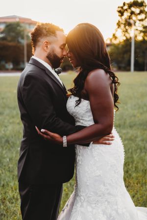 Romantic golden hour portrait of newlyweds embracing in a grassy field.