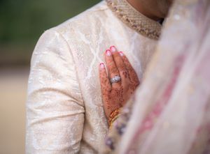 Henna-adorned hands with engagement ring against cream sherwani during wedding ceremony.