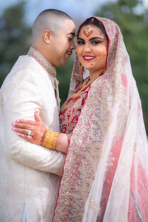 Joyful wedding couple in traditional South Asian attire sharing intimate moment.