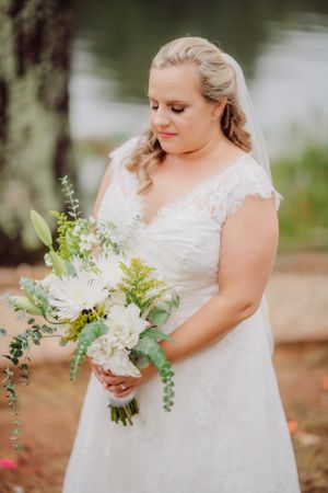 Beautiful bridal bouquet with white flowers and greenery held against a lace wedding dress.