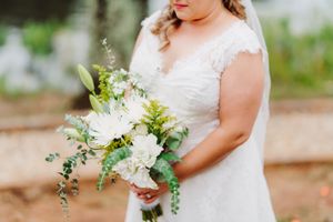 Bride holds elegant white and green floral bouquet in lace cap sleeve wedding dress.