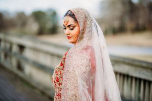 Beautiful bride in a delicate pink lace veil poses outdoors wearing traditional South Asian bridal attire.