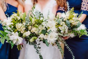 Elegant white and green wedding bouquets held by bridesmaids in navy blue dresses.
