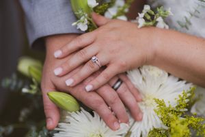 Close up of wedding rings with white flowers and greenery in the background.