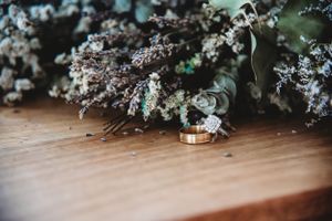 Wedding rings displayed with delicate dried flowers and greenery on a wooden surface.