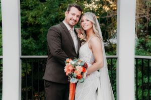 A classic wedding portrait on a white columned porch with coral floral bouquet.