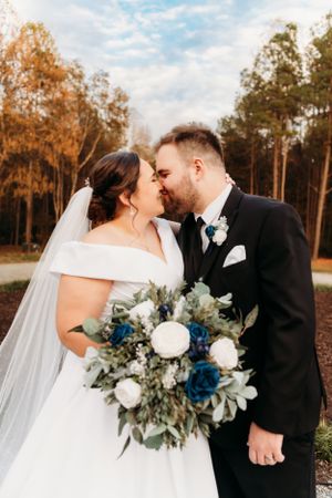 A tender moment between newlyweds with a blue and white bouquet in front of fall foliage.