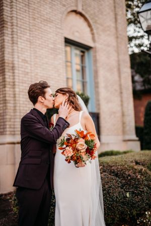 Romantic wedding photo of couple sharing intimate moment against brick church wall.