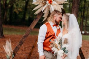 Wedding couple shares romantic moment under boho floral arch with pampas grass decor.