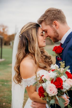 Romantic wedding portrait with bride holding red and pink rose bouquet while sharing intimate moment.