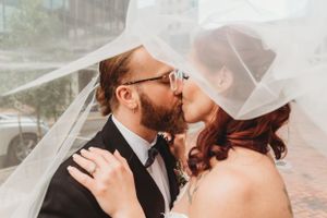 Romantic wedding kiss under flowing white veil outdoors.