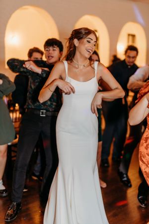 A bride in a sleek white gown dances energetically at her wedding reception.