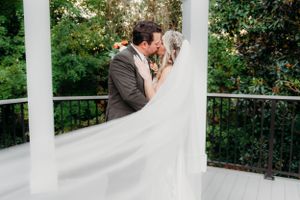 A romantic wedding kiss captured under a white gazebo surrounded by lush greenery.