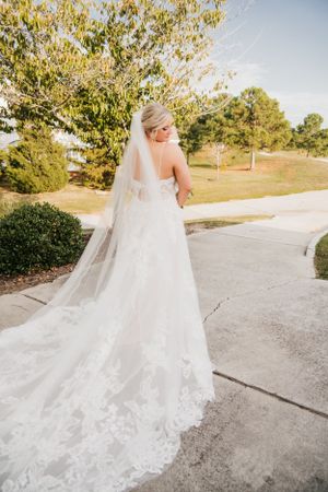 Full length back view of wedding gown with cathedral length veil on outdoor path.