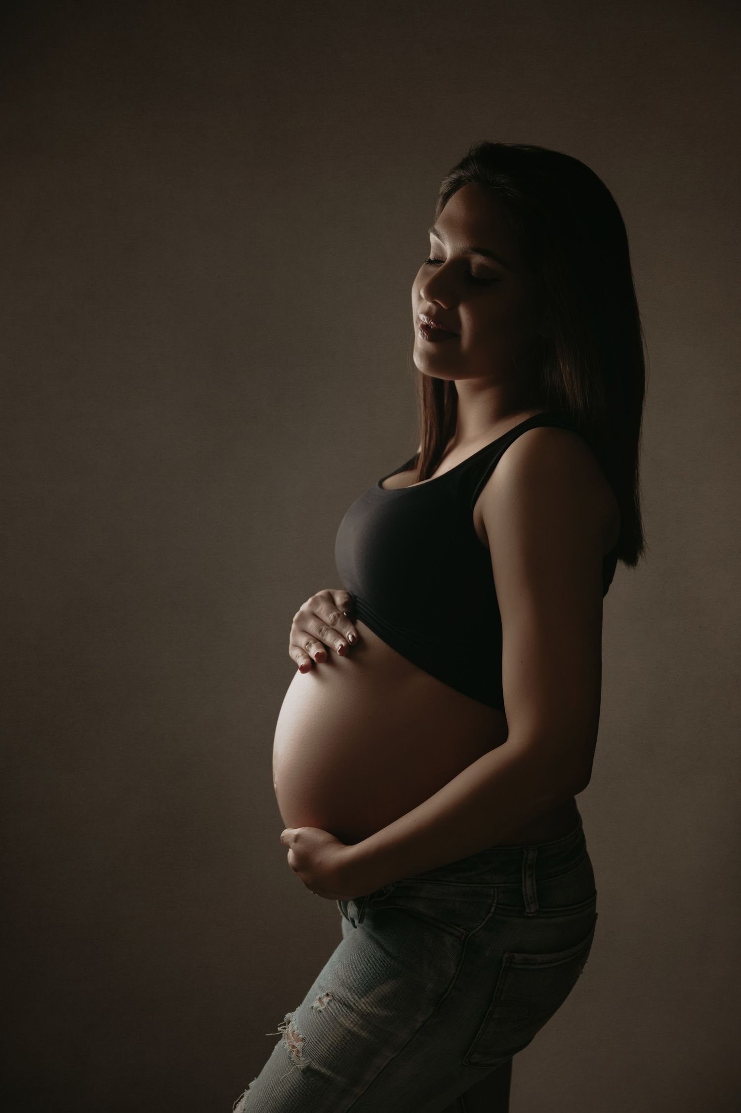 Dramatic silhouette of pregnant woman in black top against dark background.