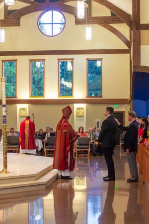 Religious ceremony in a modern church with wooden beams and tall windows illuminating the space.