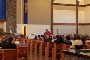 A church service in progress with congregants seated in wooden pews and a modern stone interior design.