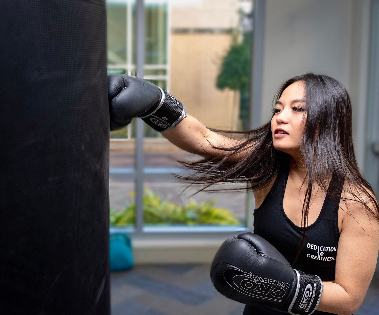 Athletic person throwing a punch at a black boxing bag while wearing boxing gloves.