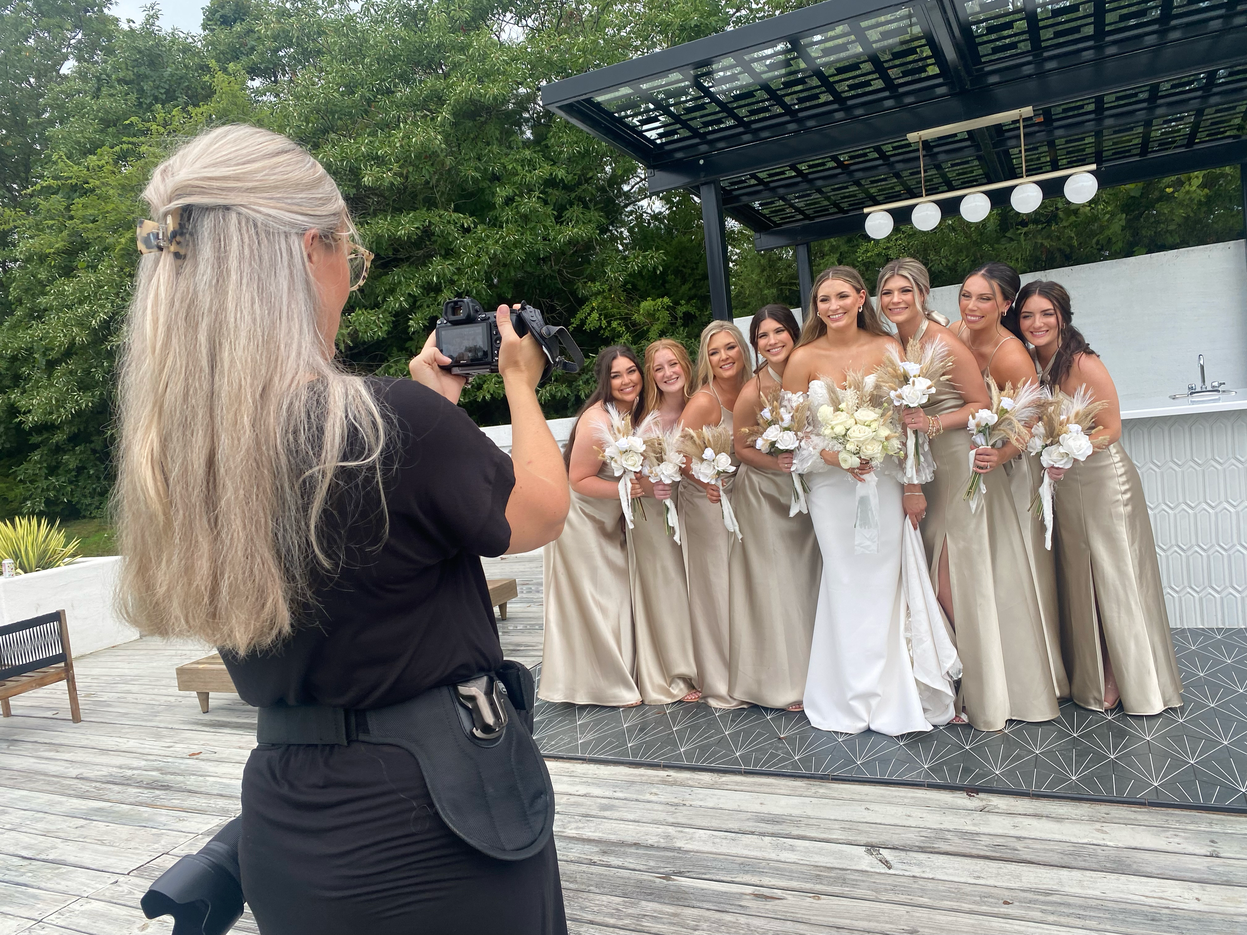 Wedding photographer captures bridal party in neutral dresses on outdoor deck.
