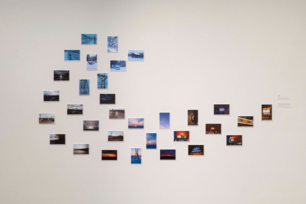 Collection of small photographs arranged in a flowing pattern across a white gallery wall.