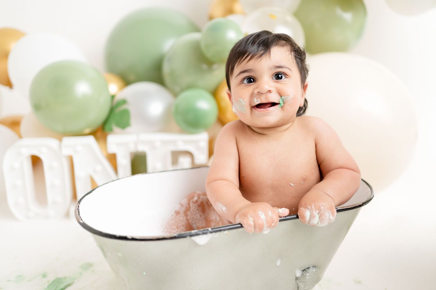Happy baby sitting in vintage white bathtub with balloon backdrop.
