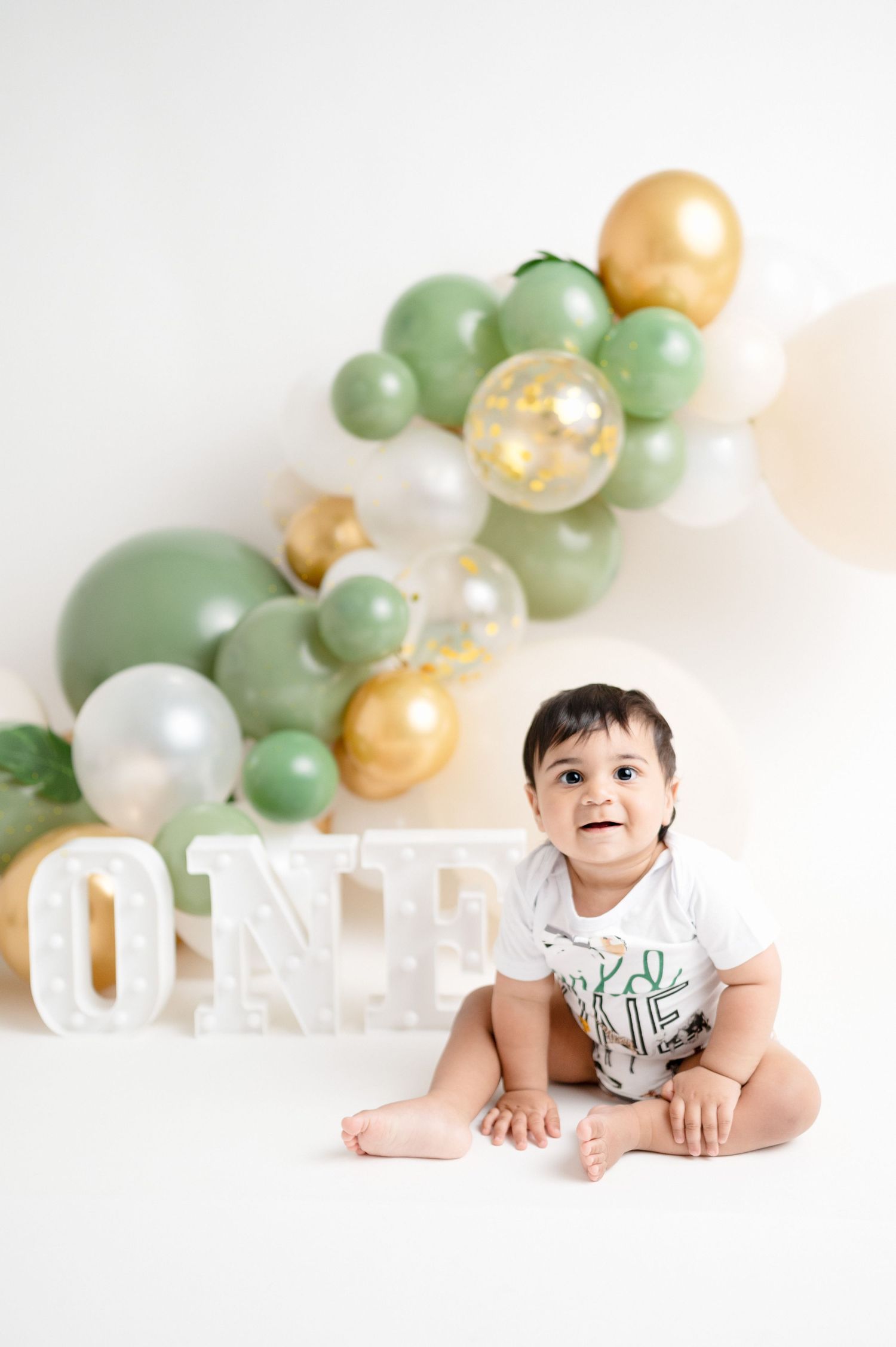 Baby sitting by ONE letter display with mint green and gold balloon arch background.