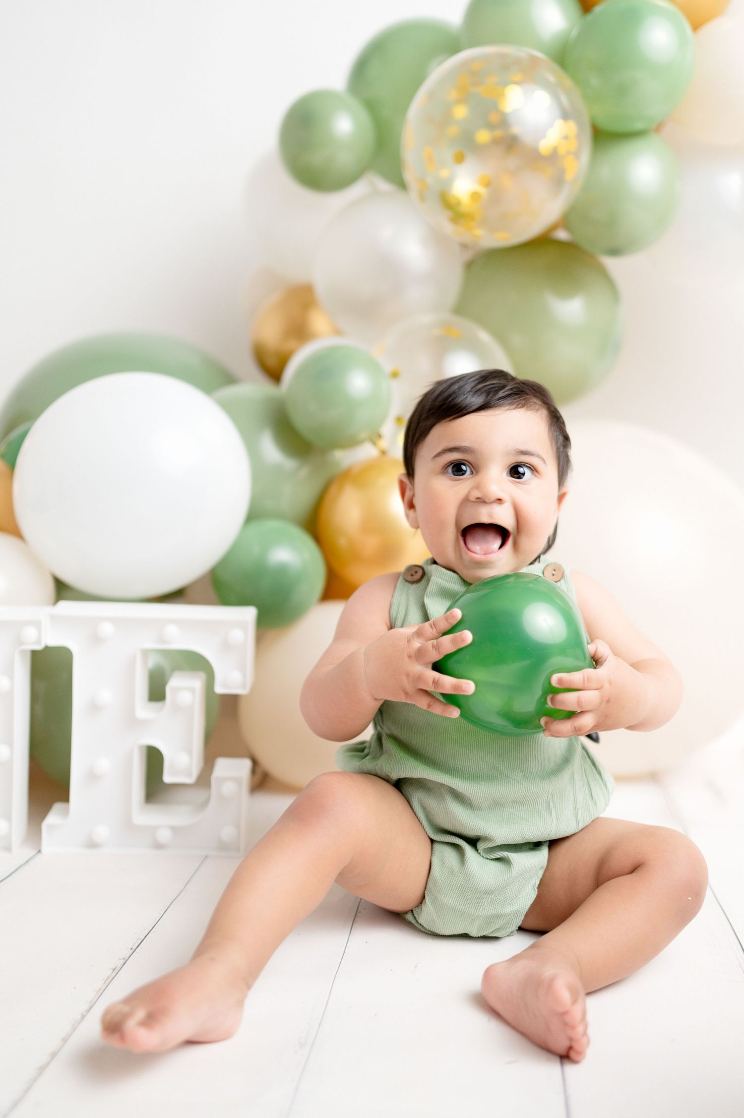 First birthday photo session with green and gold balloons and white ONE letters.