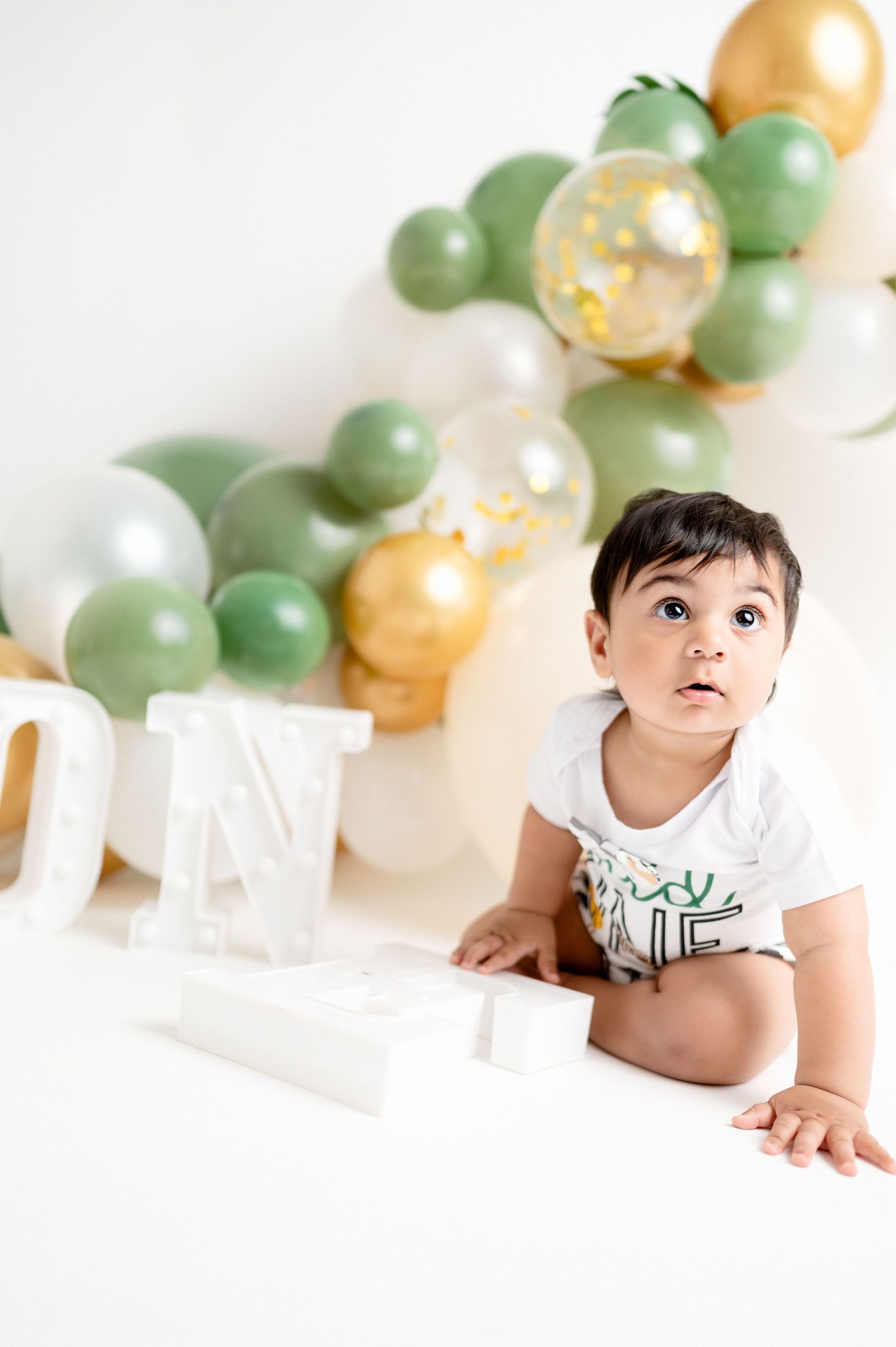A festive first birthday setup with decorative balloons in mint green and gold.
