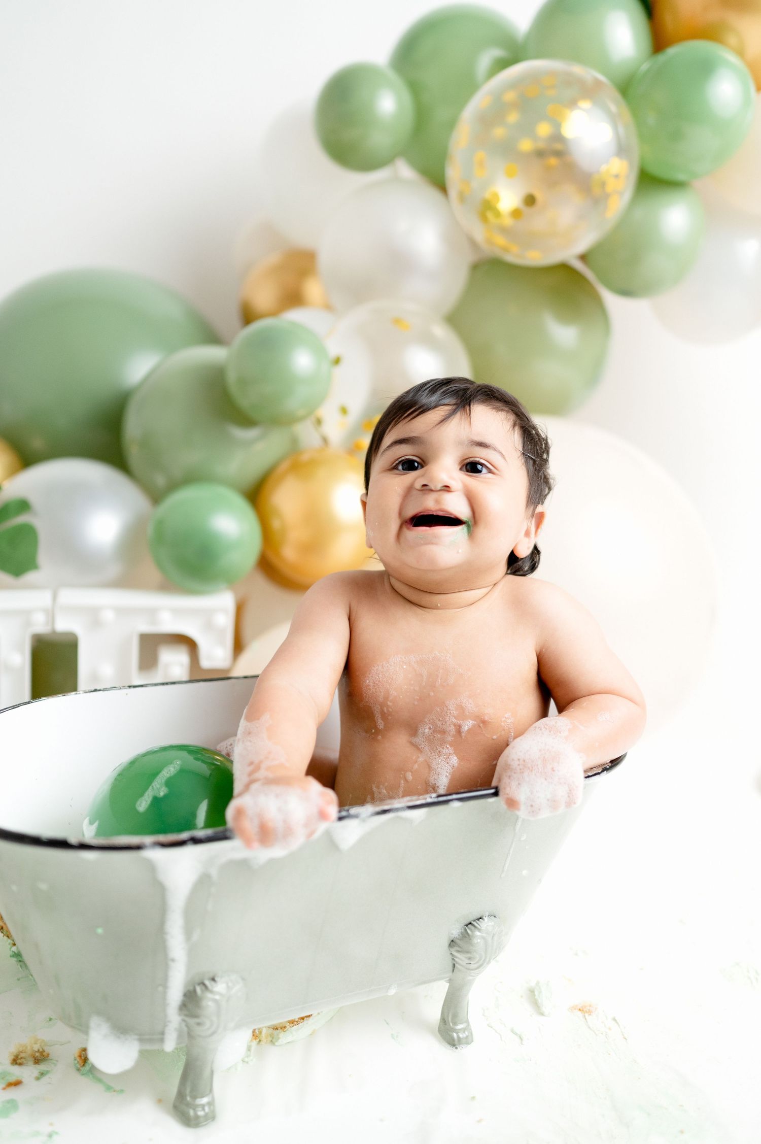 Joyful baby playing in clawfoot tub during milestone photo session.