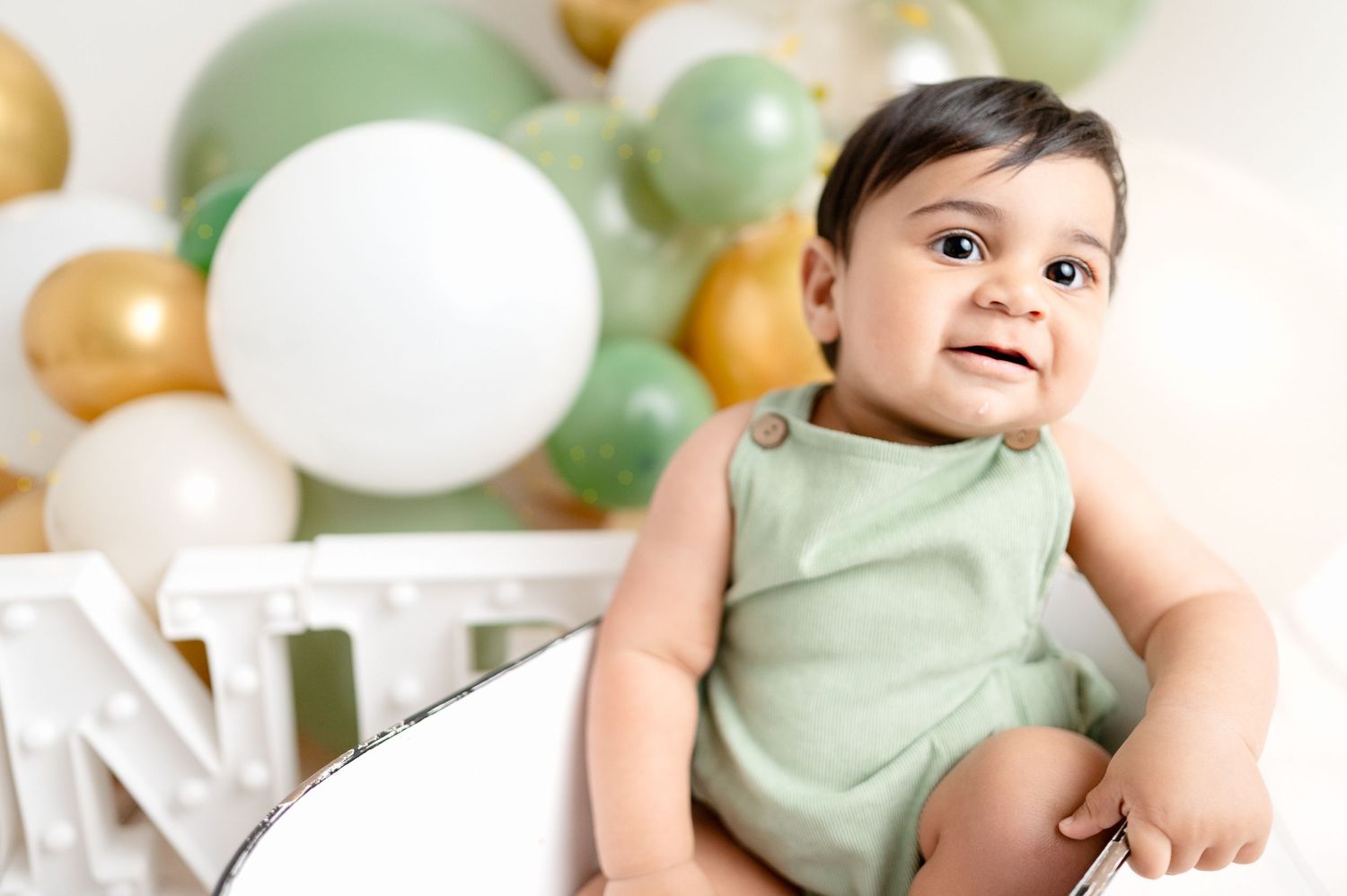 First birthday photo featuring white letters and mint green balloon decorations.