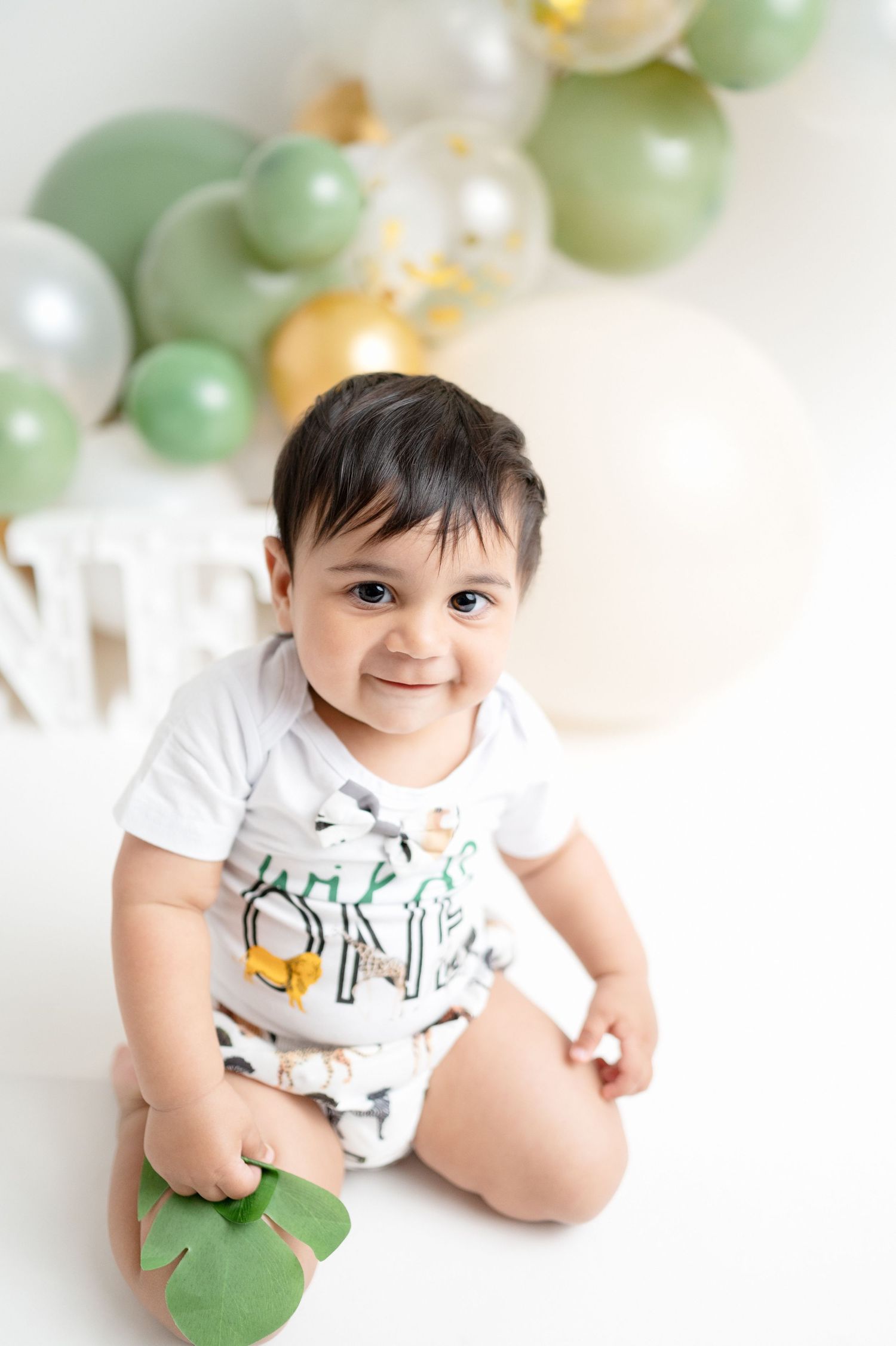 First birthday celebration setup with mint green and metallic balloon arch and decorative letters.