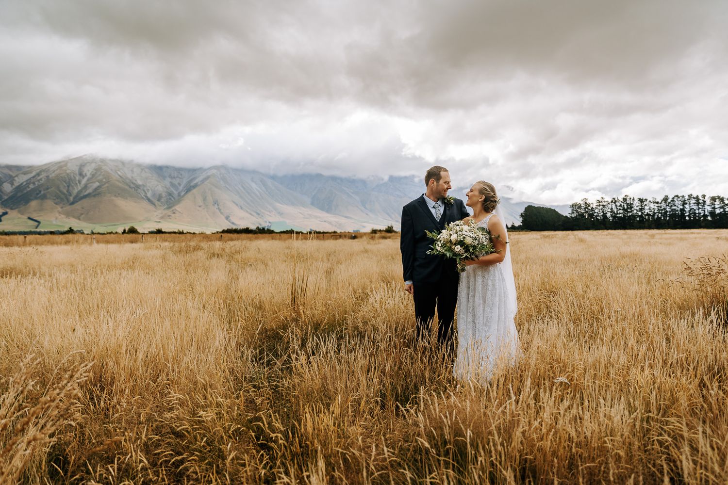 South Canterbury wedding at Fable Terrace Downs with bride and groom in long grass dark clouds and snow dusted mountains