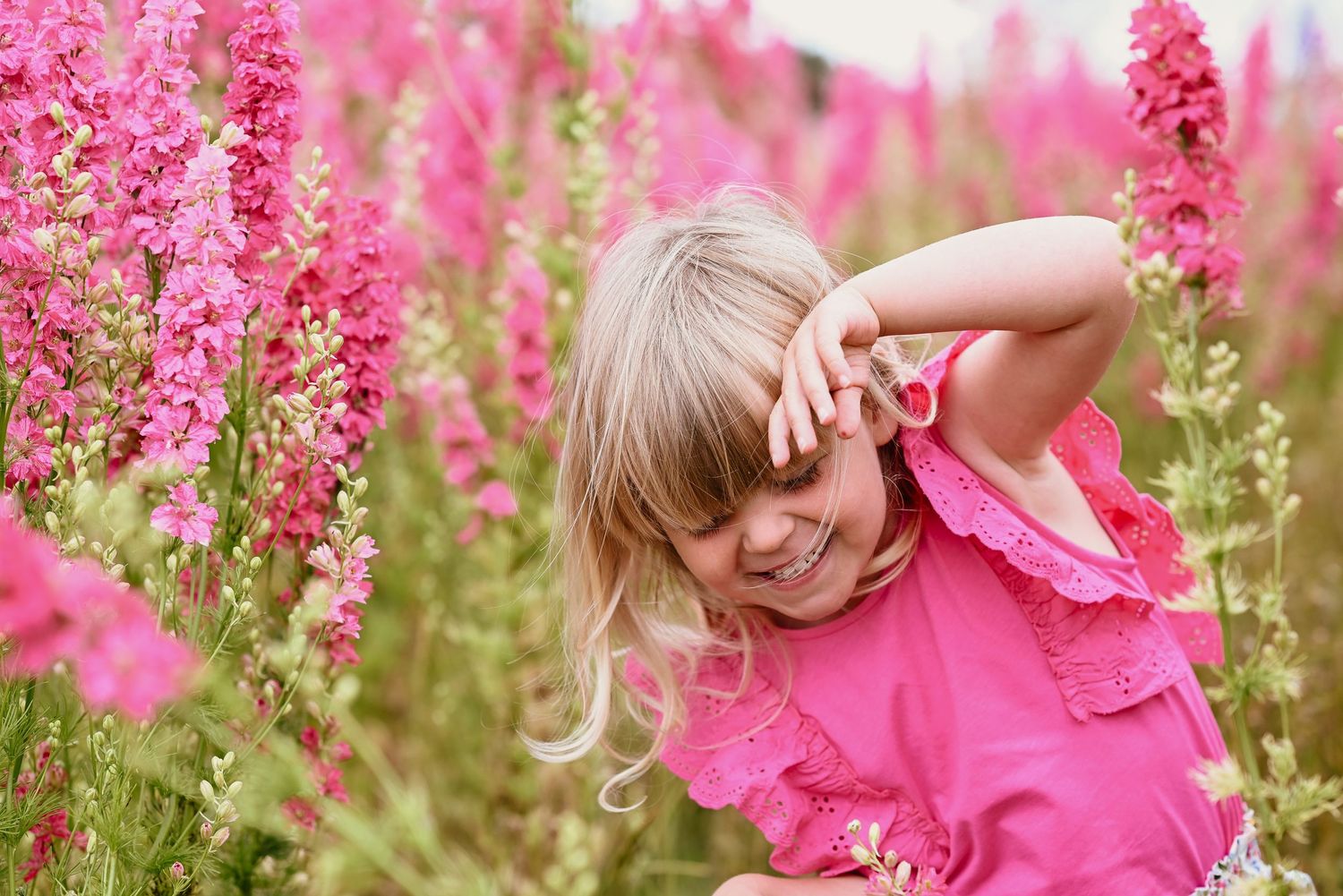 A dreamy summer scene in a field of bright pink flowers with someone in a matching pink outfit enjoying nature.