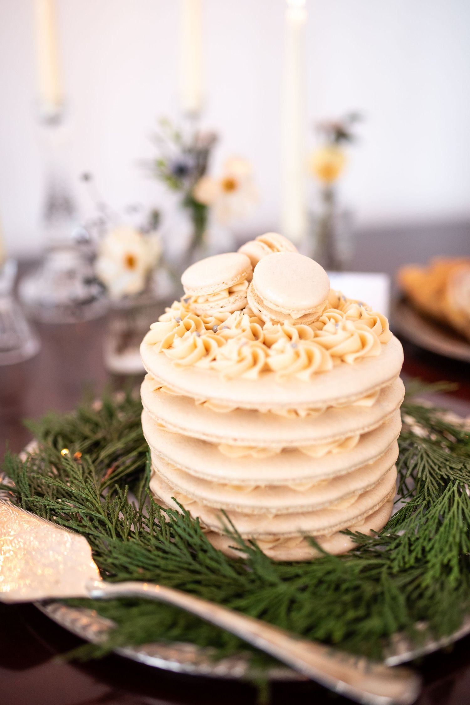 Layered white macaron cake decorated with evergreen sprigs on silver platter.