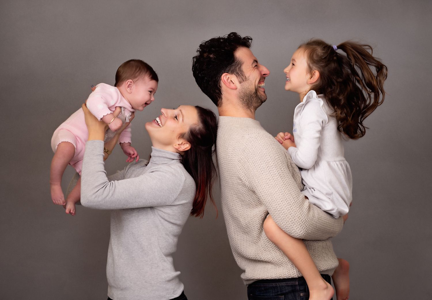 A family in matching light-colored outfits plays and laughs together during a studio photoshoot.