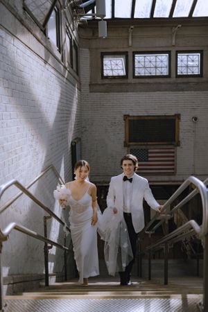 A wedding couple ascending stairs in an industrial-style building with white brick walls.