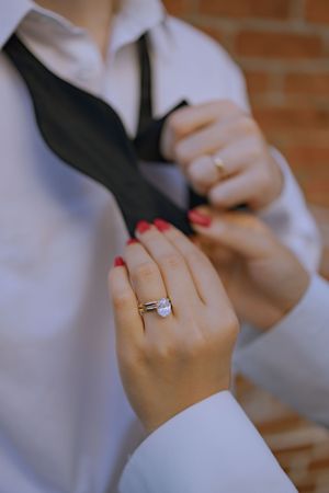 Close-up of hands adjusting a black tie with an engagement ring visible.