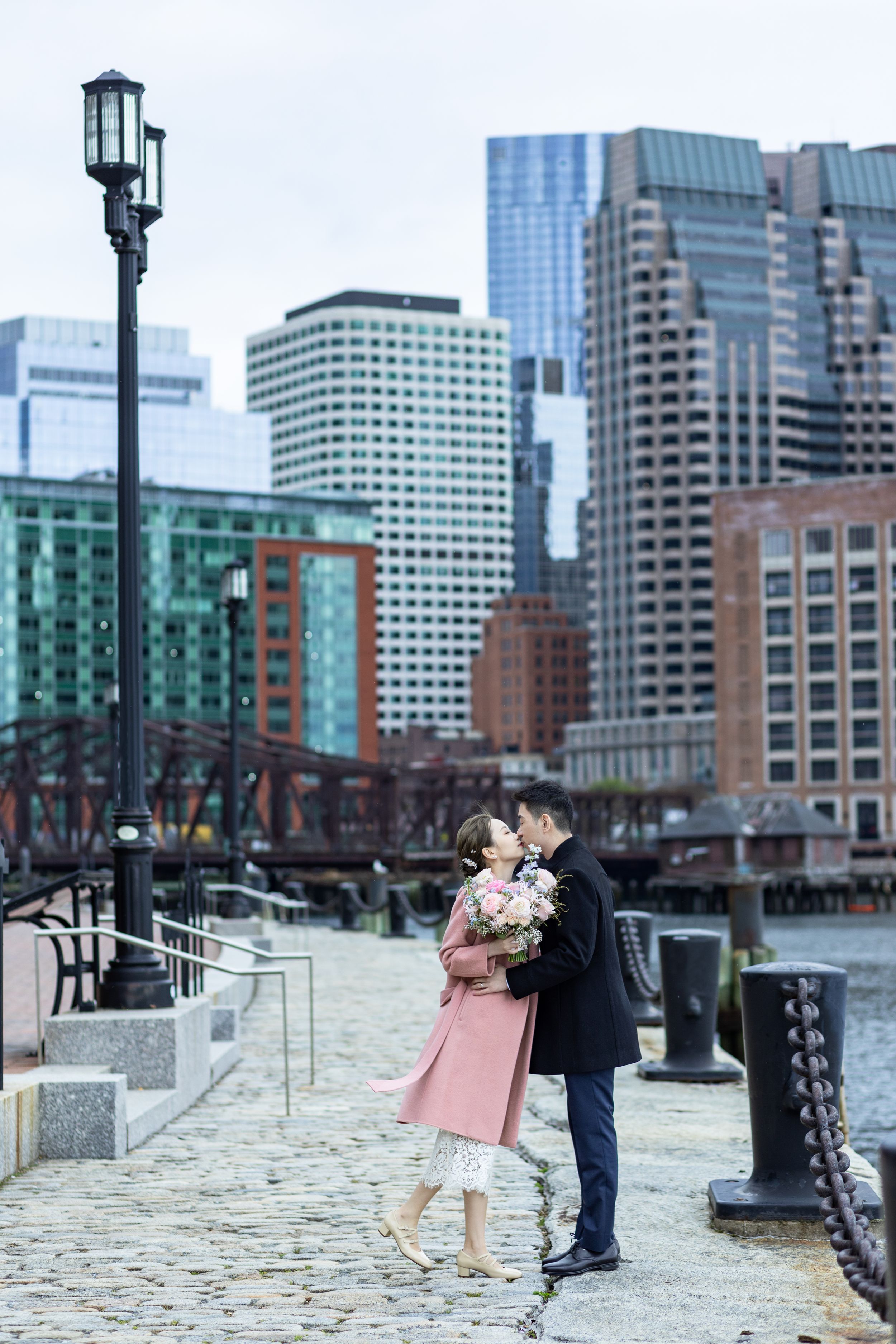 Romantic engagement photoshoot on a stone walkway with city skyline in the background.