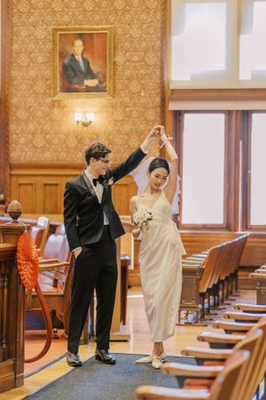 Playful wedding photos in a formal room with orange walls and wooden pews.