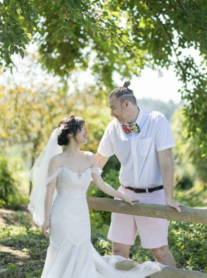 A romantic wedding photo of a couple in a garden setting with green foliage and natural sunlight.