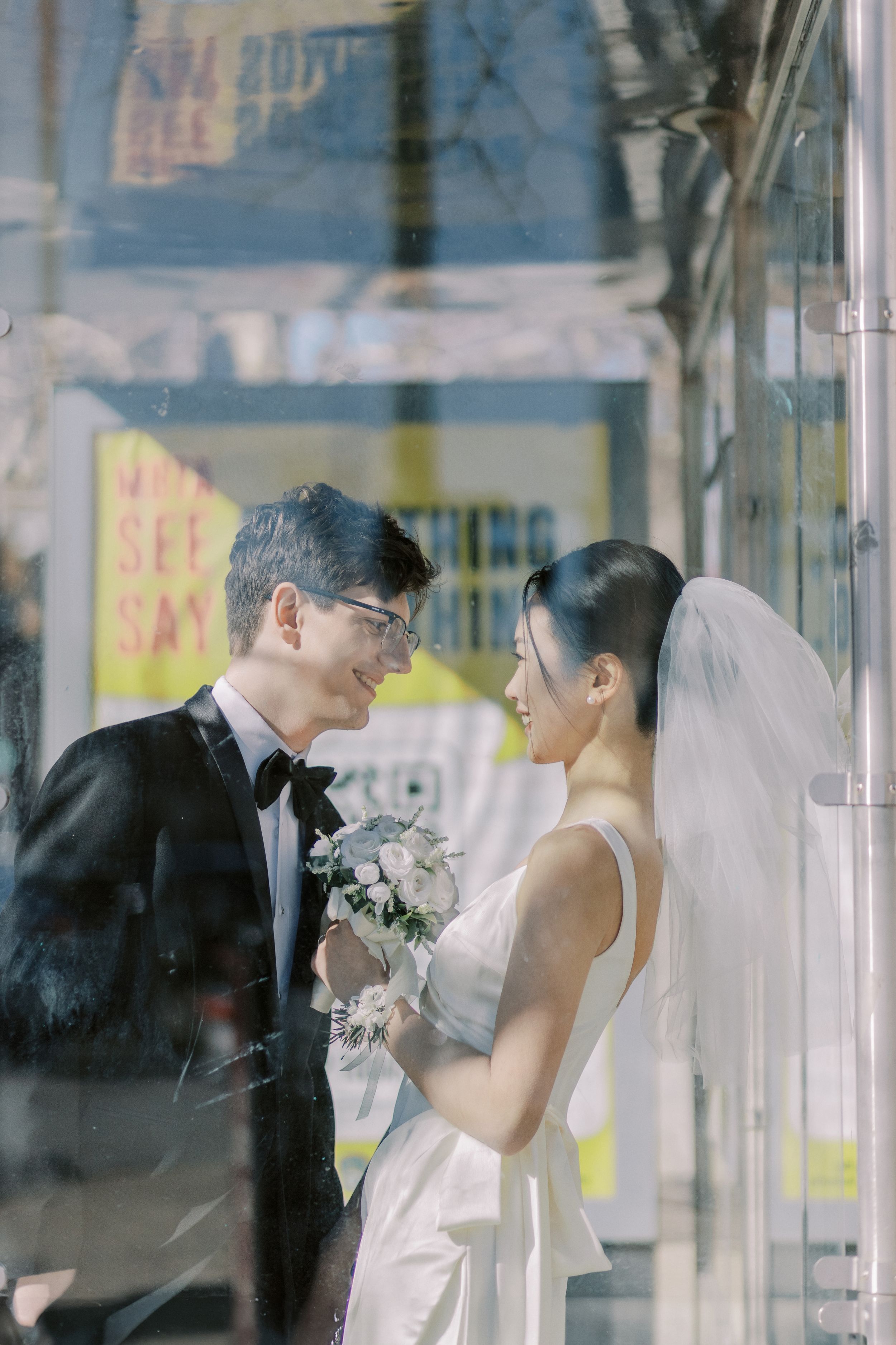 An intimate wedding portrait through glass showing a couple in formal attire with reflections.