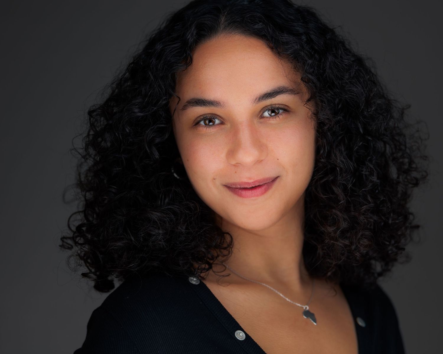 Studio portraits of a smiling woman with natural curly hair against dark backdrop.