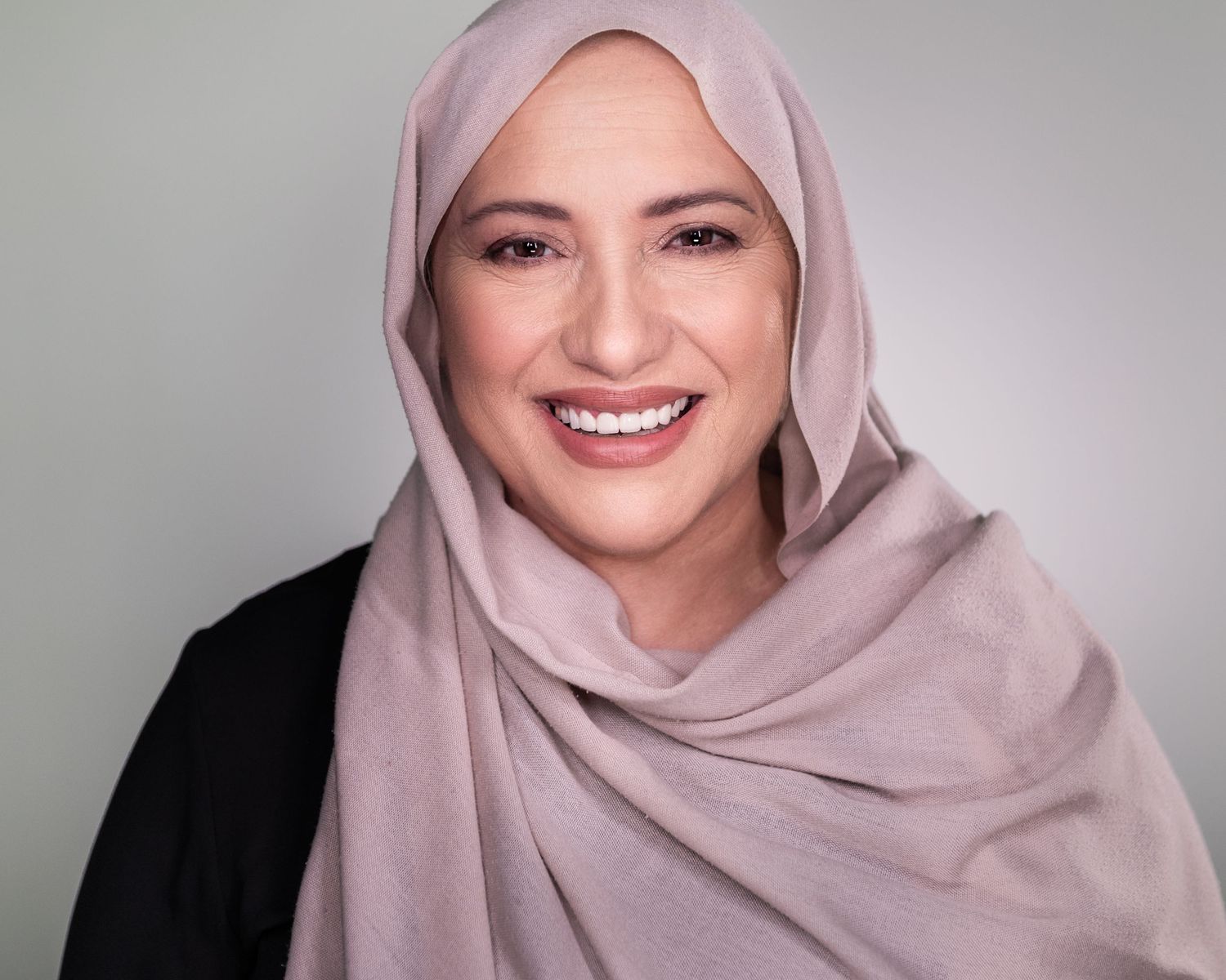 Studio portraits featuring person in light pink hijab and black outfit against light background.