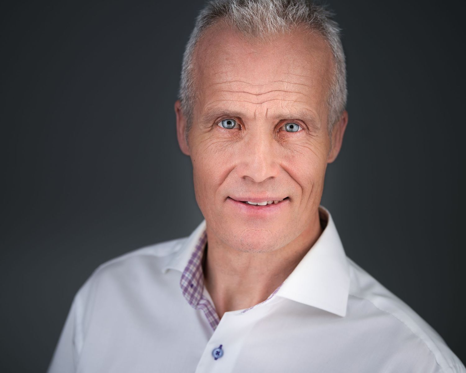 Studio portraits of person in white dress shirt and purple tie against dark background.