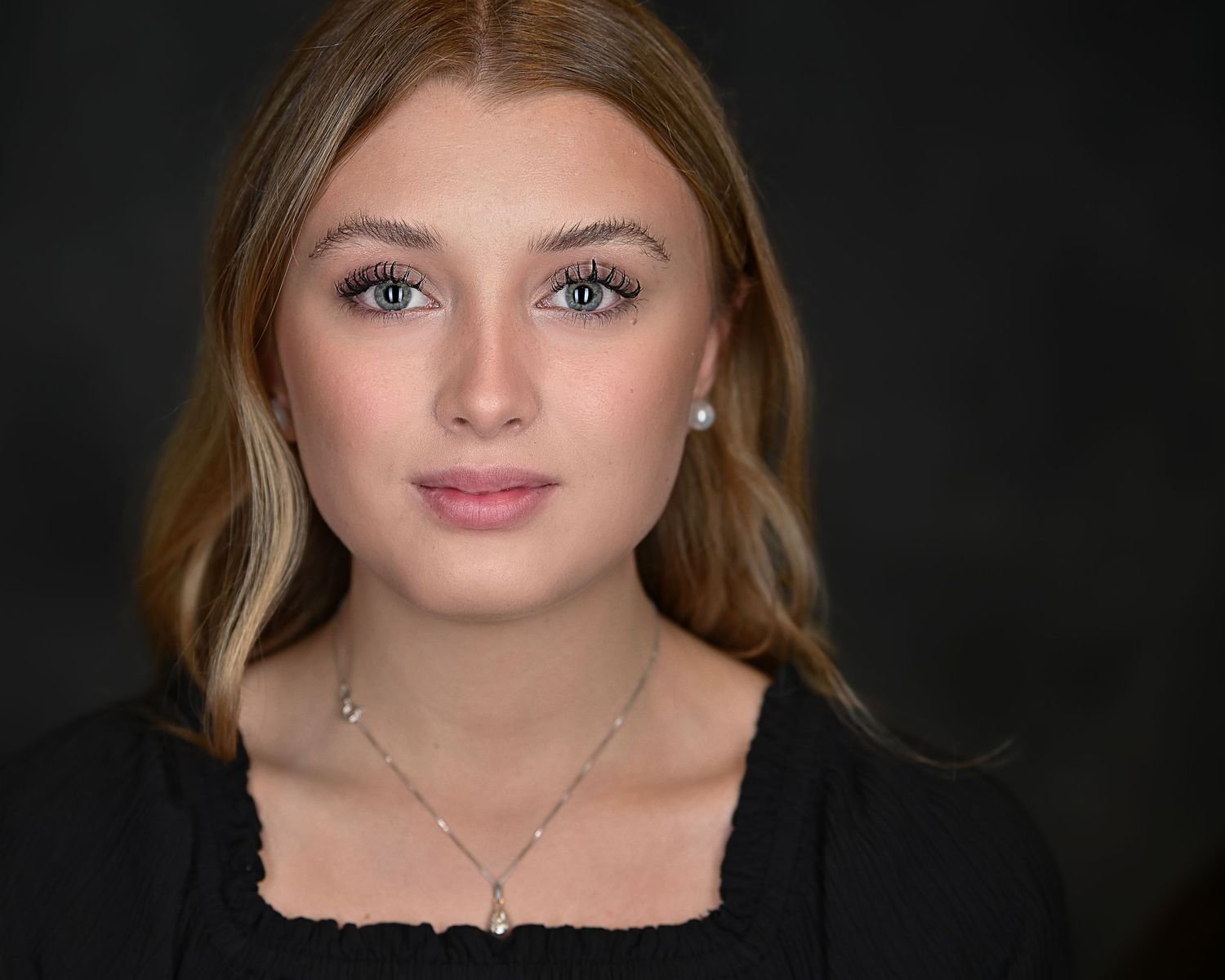 Close-up beauty portrait of young woman wearing black top with delicate necklace.