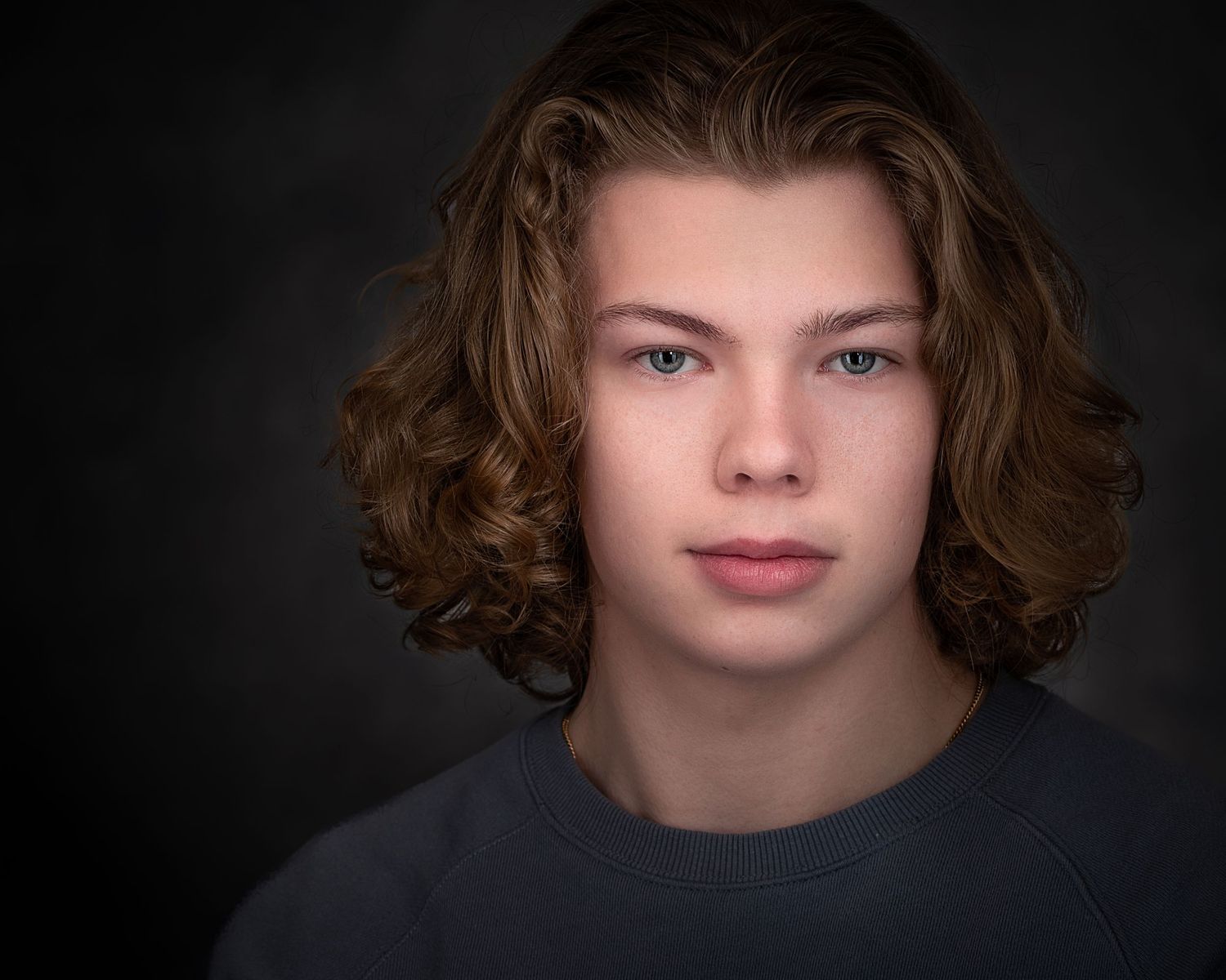 Dramatic portrait of young person with wavy brown hair wearing dark sweater.