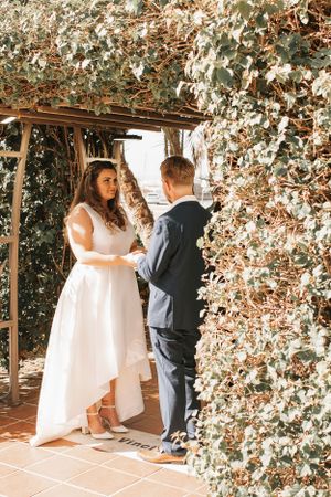 Wedding couple dancing under a pergola decorated with white flowers and greenery.
