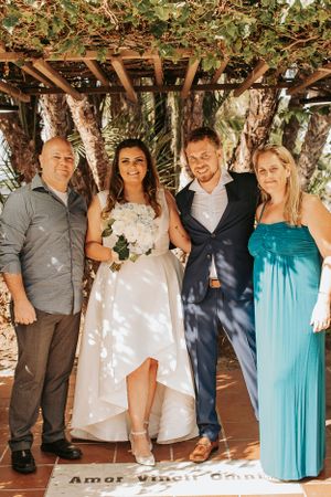 Wedding party poses together under a floral-covered pergola in formal attire.